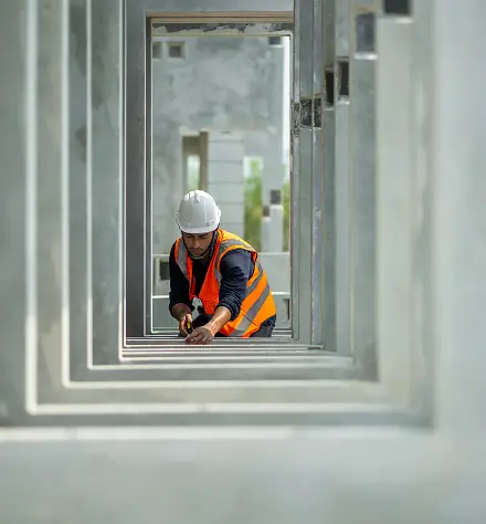 A construction worker wearing a hard hat and safety vest stands inside an office building, surveying the work area.