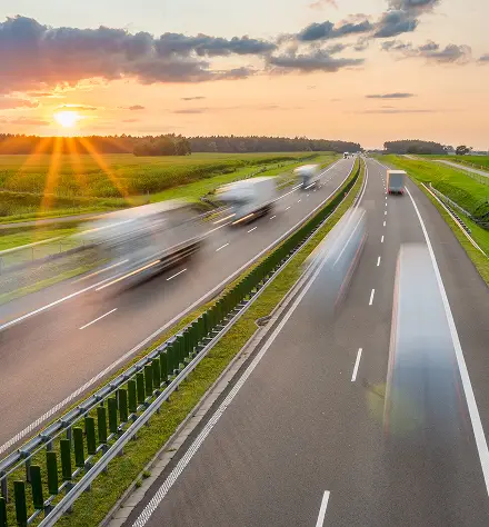 A sunset casts a warm glow over a highway, with cars traveling along the road under the colorful sky.