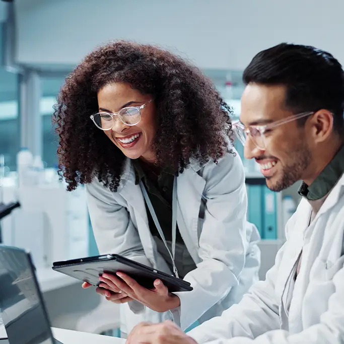 Two individuals in lab coats examining a laptop screen together in a laboratory setting.