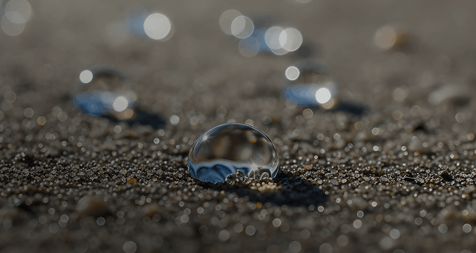 Close-up of water droplets glistening on a sandy surface, highlighting the contrast between moisture and dry sand.
