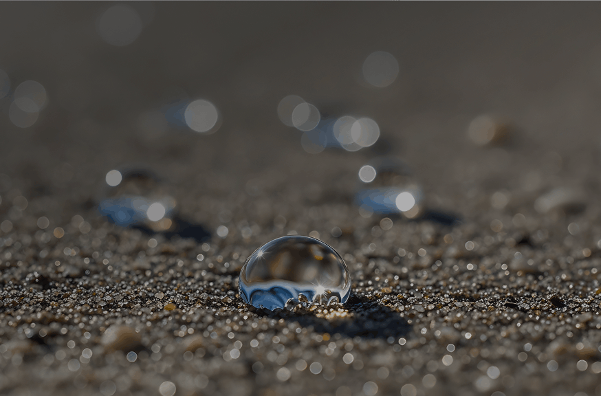 Close-up of water droplets glistening on a sandy surface, highlighting the contrast between moisture and dry sand.