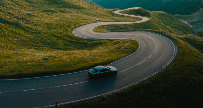 A car navigates a winding mountain road, surrounded by lush greenery and steep cliffs.
