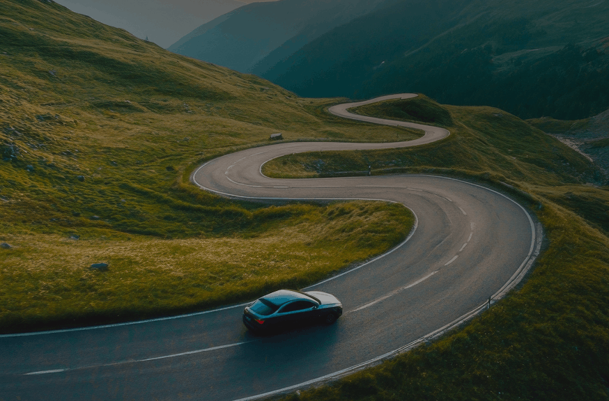 A car navigates a winding mountain road, surrounded by lush greenery and steep cliffs.