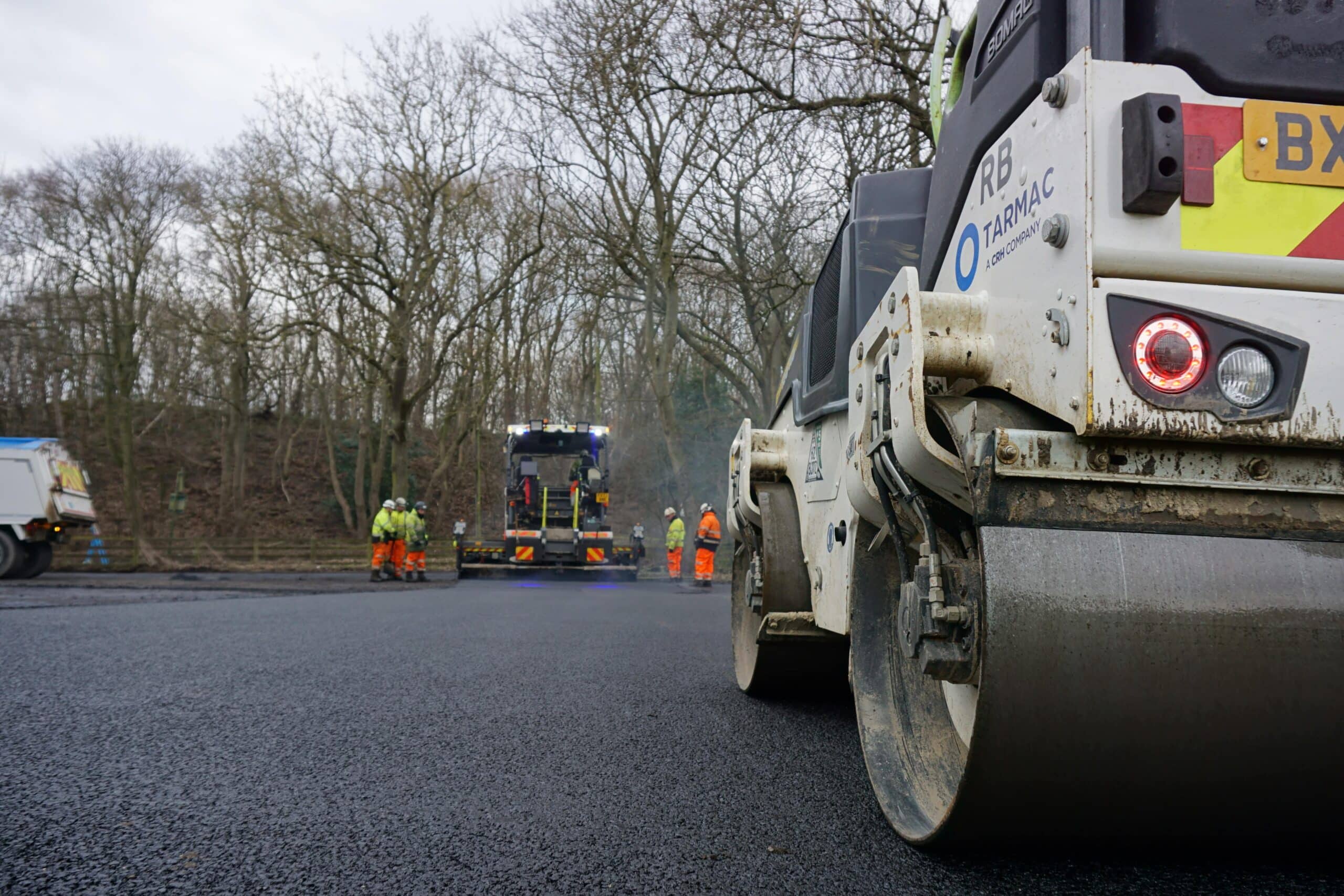 A large construction vehicle is actively working on a road, surrounded by construction materials and equipment.